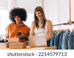Small photo of Cheerful businesswomen using a laptop while preparing an online order in a thrift store. Happy small business owners making plans for a shipment. Female entrepreneurs running an online clothing store.
