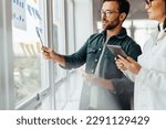 Small photo of Creative business people brainstorming with sticky notes in an office. Business professionals standing next to a window and discussing their ideas.