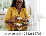 Small photo of Happy mature woman sitting at her kitchen table and taking daily medication to manage a chronic condition. Woman adhering to her prescribed treatment plan to maintain her health and quality of life.