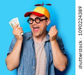 Small photo of Young nerd man with noob hat holding a money on blue background