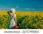 Beautiful woman in dress with suitcase in rapeseed field in spring time 