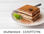 Delicious Tiramisu cake with coffee beans and fresh mint on a plate on a light background.