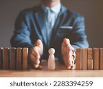 Small photo of Risk management and assessment concept. Businessman prevent or protect his business and employee from high risk. Wood block represent of risk attack to business, two hands block and protect the domino