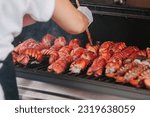 Small photo of torso of cook in apron and glove brushing butter on lobster tails on a hot outdoor grill at event