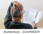 Small photo of Worried middle-aged man reading unexpected news in paper document. He is confused and astonished by unbelievable news: high bill tax invoice, debt notification, bad financial report, money problem