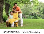 Happy Indian healthy family sitting in a city park bench having a cheerful time together. They are surrounded with greenery and serene atmosphere in peaceful and calm environment.