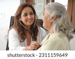 Small photo of Attractive young Indian doctor sitting with senior patient. Doctor giving consultation to an elderly woman. An elderly patient having a routine checkup from a family doctor. Elderly patient diagnosis.