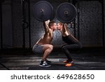 Young beautiful sportive woman and man kissing and lifting a dumbbell from squats against brick wall in the gym.