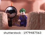 Small photo of Tangsel, Indonesia - May 20, 2021: Joker lego minifig with "don't care" expression stand next bat signal and with little mist effect. lego minifigs are made by the lego group.