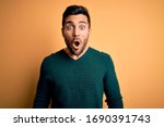 Young handsome man with beard wearing casual sweater standing over yellow background afraid and shocked with surprise expression, fear and excited face.