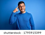 Young handsome man with beard wearing casual sweater and glasses over blue background Smiling pointing to head with one finger, great idea or thought, good memory