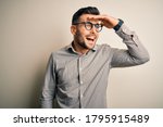 Young handsome man wearing elegant shirt and glasses over isolated white background very happy and smiling looking far away with hand over head. Searching concept.