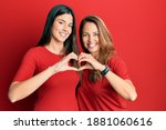Hispanic family of mother and daughter wearing casual clothes over red background smiling in love doing heart symbol shape with hands. romantic concept. 