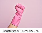 Hand of caucasian young man with cleaning glove over isolated pink background doing protest and revolution gesture, fist expressing force and power
