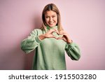 Young beautiful blonde woman wearing winter wool sweater over pink isolated background smiling in love doing heart symbol shape with hands. Romantic concept.