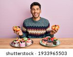 Young handsome man holding sweet pastries smiling and laughing hard out loud because funny crazy joke. 