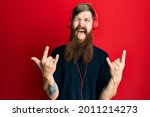 Redhead man with long beard listening to music using headphones shouting with crazy expression doing rock symbol with hands up. music star. heavy concept. 