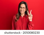 Young latin woman wearing casual clothes and glasses showing and pointing up with fingers number two while smiling confident and happy. 