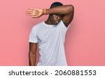 Small photo of Young african american man wearing casual white t shirt covering eyes with arm, looking serious and sad. sightless, hiding and rejection concept