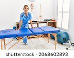 Small photo of Young caucasian physio therapist smiling happy leaning on table at the clinic