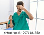 Small photo of Young hispanic doctor man holding covid record card covering eyes with hand, looking serious and sad. sightless, hiding and rejection concept