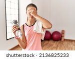 Small photo of Young brunette teenager wearing sportswear holding water bottle covering eyes with hand, looking serious and sad. sightless, hiding and rejection concept