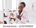 Small photo of African american woman wearing doctor uniform holding anatomical model of uterus with fetus at clinic
