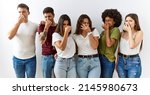 Small photo of Group of young friends standing together over isolated background smelling something stinky and disgusting, intolerable smell, holding breath with fingers on nose. bad smell