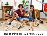 Small photo of Young hispanic couple doing laundry with dogs smelling something stinky and disgusting, intolerable smell, holding breath with fingers on nose. bad smell