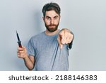 Small photo of Caucasian man with beard holding pocket knife pointing with finger to the camera and to you, confident gesture looking serious