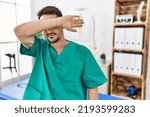 Small photo of Young physiotherapist man working at pain recovery clinic covering eyes with arm, looking serious and sad. sightless, hiding and rejection concept