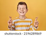 Small photo of Young caucasian kid standing over yellow background gesturing finger crossed smiling with hope and eyes closed. luck and superstitious concept.