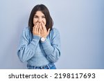 Small photo of Young hispanic woman standing over blue background laughing and embarrassed giggle covering mouth with hands, gossip and scandal concept