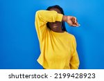Small photo of Beautiful black woman standing over blue background covering eyes with arm, looking serious and sad. sightless, hiding and rejection concept