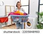 Middle age hispanic woman holding laundry basket smiling with a happy and cool smile on face. showing teeth. 