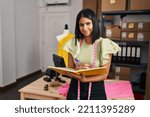 Small photo of Young latin woman dressmaker writing on book at designer studio