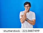 Small photo of Handsome latin man standing over blue background smelling something stinky and disgusting, intolerable smell, holding breath with fingers on nose. bad smell