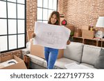 Small photo of Young latin woman smiling confident holding house plan at hew home