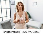 Small photo of Middle age woman drinking a cup coffee at home skeptic and nervous, frowning upset because of problem. negative person.