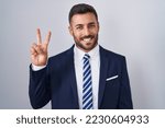 Handsome hispanic man wearing suit and tie showing and pointing up with fingers number two while smiling confident and happy. 