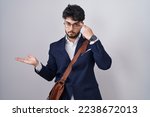 Hispanic man with beard wearing business clothes confused and annoyed with open palm showing copy space and pointing finger to forehead. think about it. 
