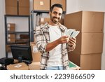 Small photo of Young hispanic man ecommerce business worker counting dollars at office