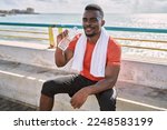 Young african american man wearing sportswear holding water bottle at seaside
