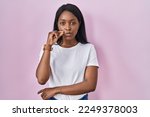 Small photo of African young woman wearing casual white t shirt mouth and lips shut as zip with fingers. secret and silent, taboo talking