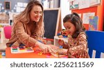 Small photo of Teacher and toddler playing with maths puzzle game sitting on table at kindergarten