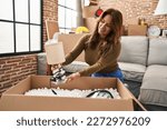 Small photo of Young latin woman smiling confident unboxing package at hew home