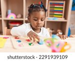Small photo of African american girl playing with maths puzzle game sitting on table at kindergarten