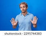 Small photo of Caucasian man standing over blue background moving away hands palms showing refusal and denial with afraid and disgusting expression. stop and forbidden.