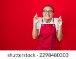 Small photo of Young hispanic woman wearing waitress apron over red background gesturing finger crossed smiling with hope and eyes closed. luck and superstitious concept.