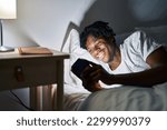African american man using smartphone lying on bed at bedroom